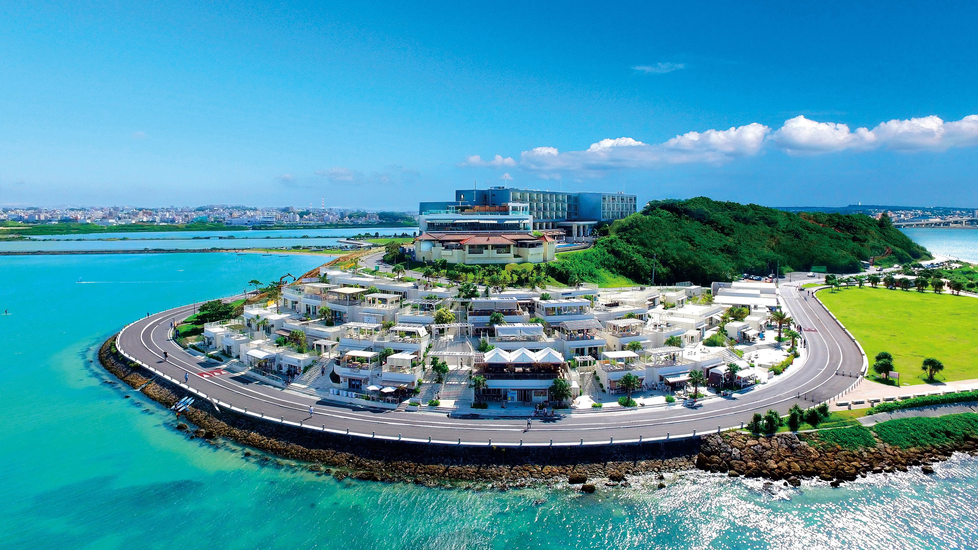 Senagajima Umikaji Terrace in okinawa, Japan - A scenic seaside complex on Senaga Island featuring white Mediterranean-style buildings cascading down hillsides, offering trendy shops, restaurants, and spectacular sunset views of aircraft landing at nearby Naha Airport